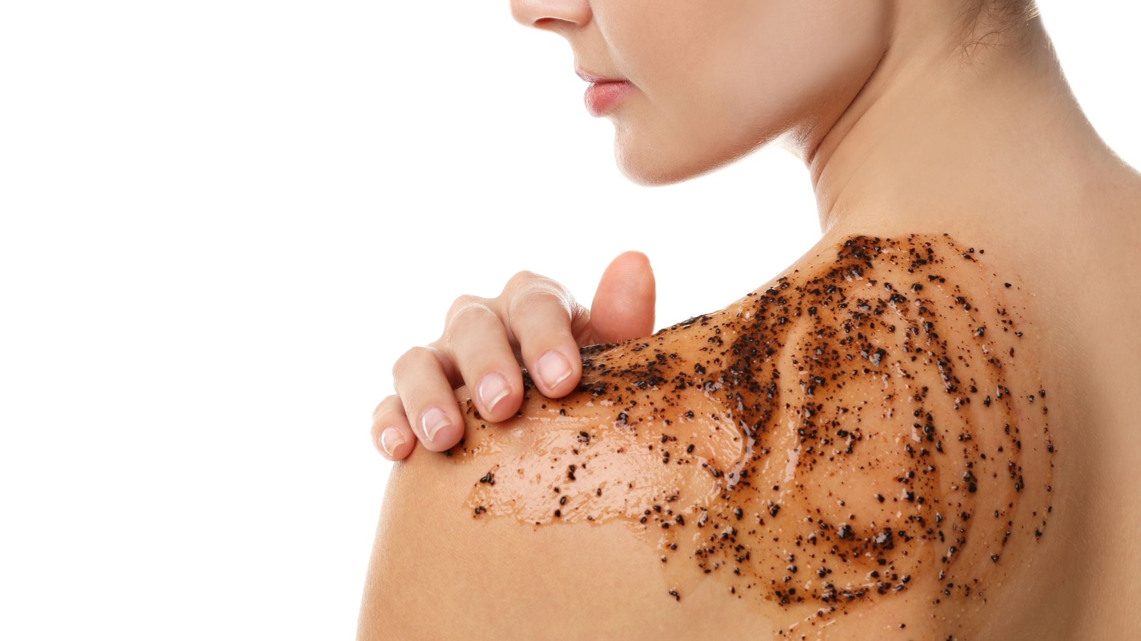 Close-up of woman applying dark granular body scrub to upper back and shoulder